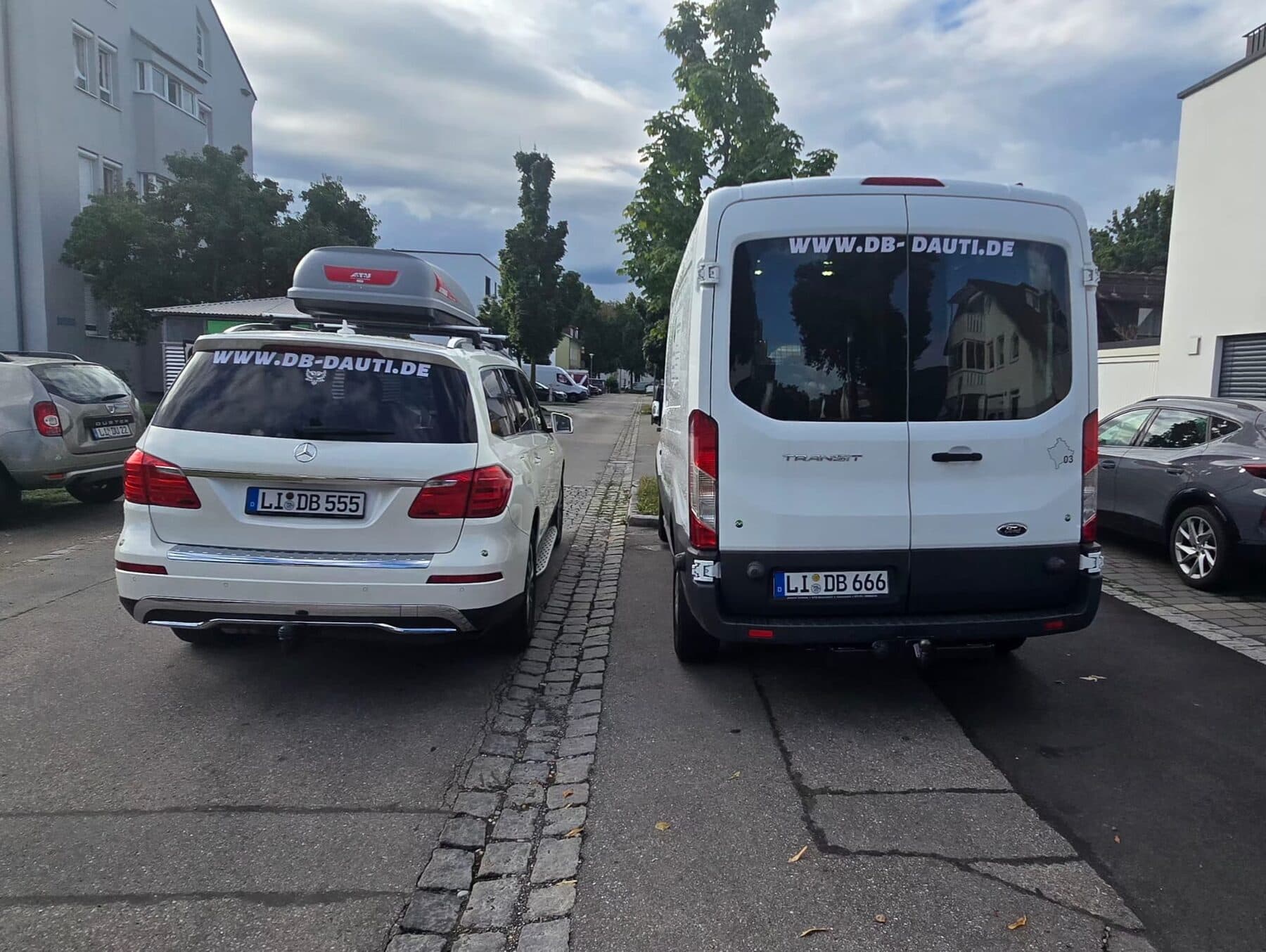Zwei weiße Fahrzeuge von D&B Dauti mit der Aufschrift www.db-dauti.de und Lindauer Kennzeichen, in einer Wohnstraße abgestellt